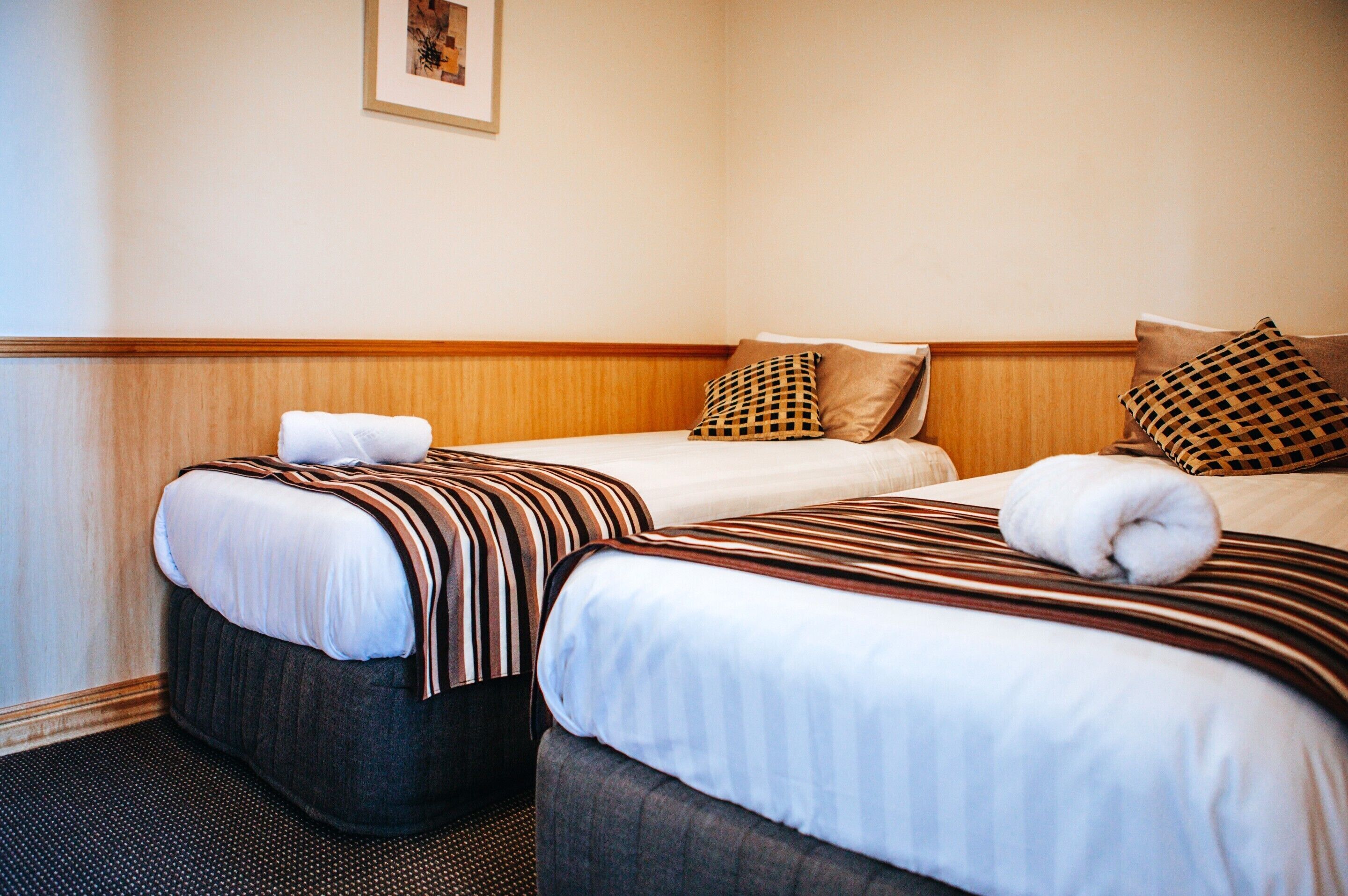 Habitación de hotel con dos camas, cada una con ropa de cama y almohadas a rayas, cabeceros de madera y un cuadro en la pared.