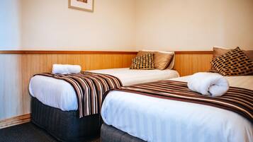 Habitación de hotel con dos camas, cada una con ropa de cama y almohadas a rayas, cabeceros de madera y un cuadro en la pared.