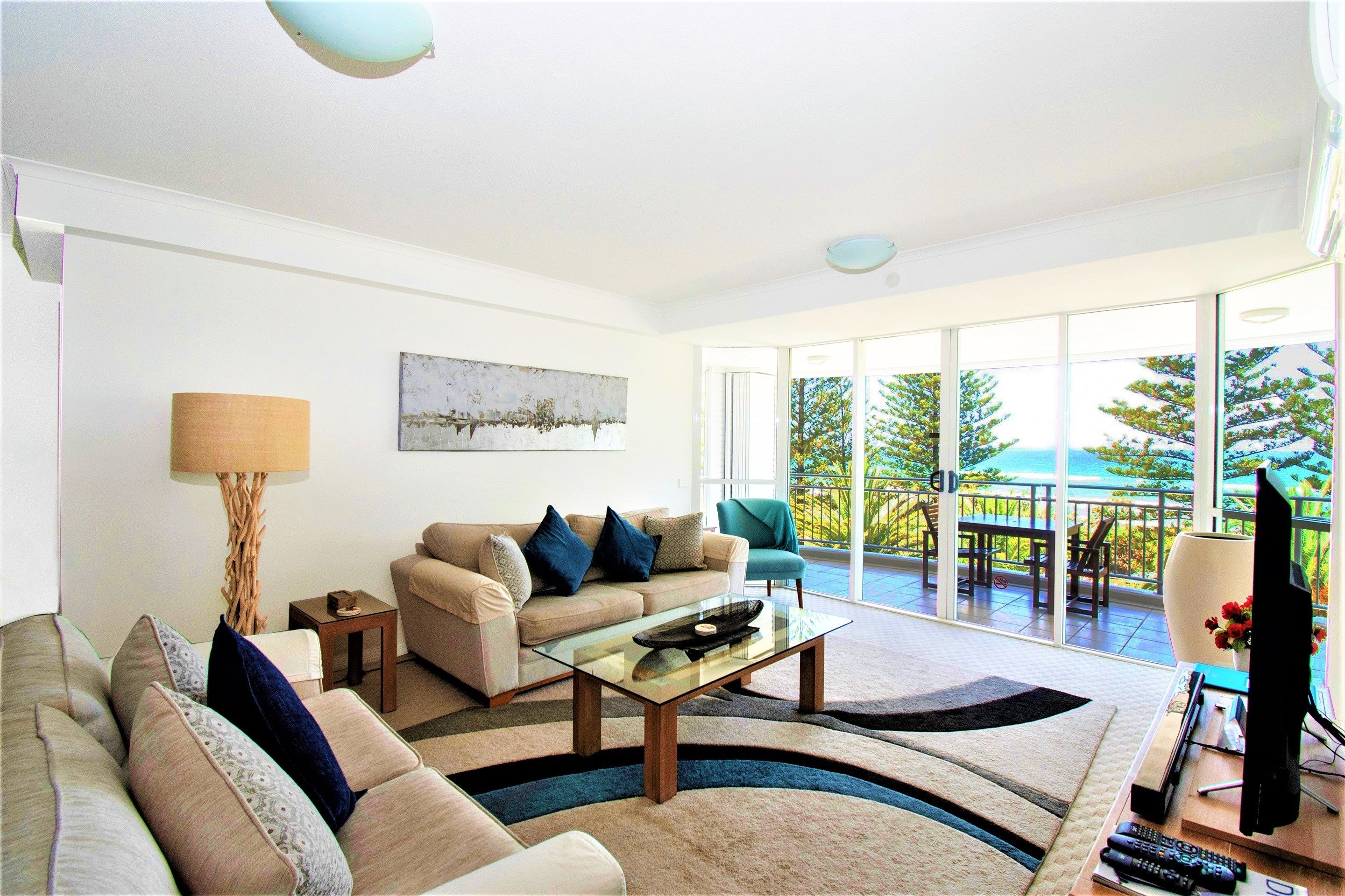 A modern living room with a sofa, coffee table, and a view of the outdoors through large sliding glass doors.