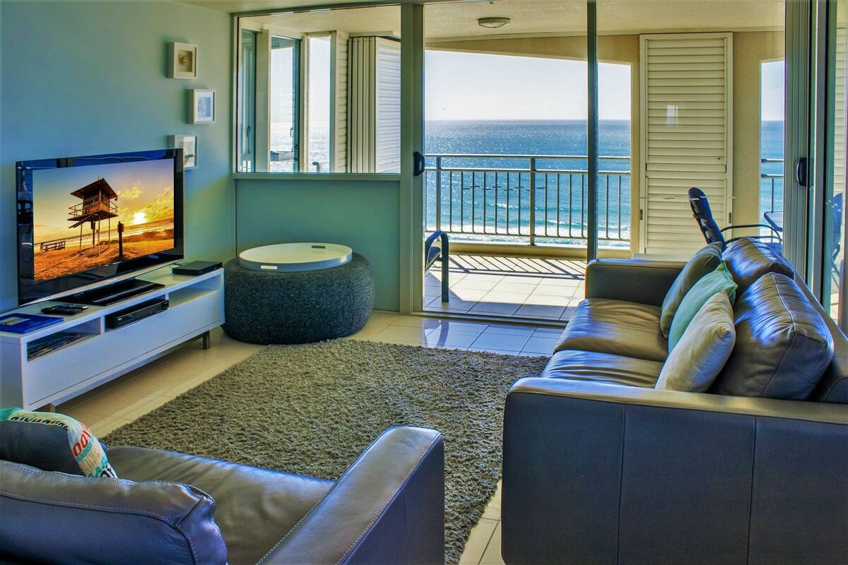 Sala de estar com televisão, sofá e vista para o oceano.