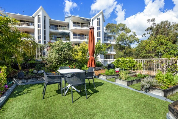Ein modernes Gebäude mit mehreren Balkonen und einem gepflegten Garten mit einer Terrassenfläche.