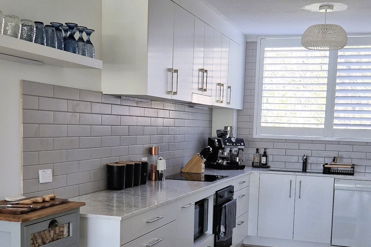 A modern kitchen with white cabinetry, a herringbone wood floor, and a striped rug.