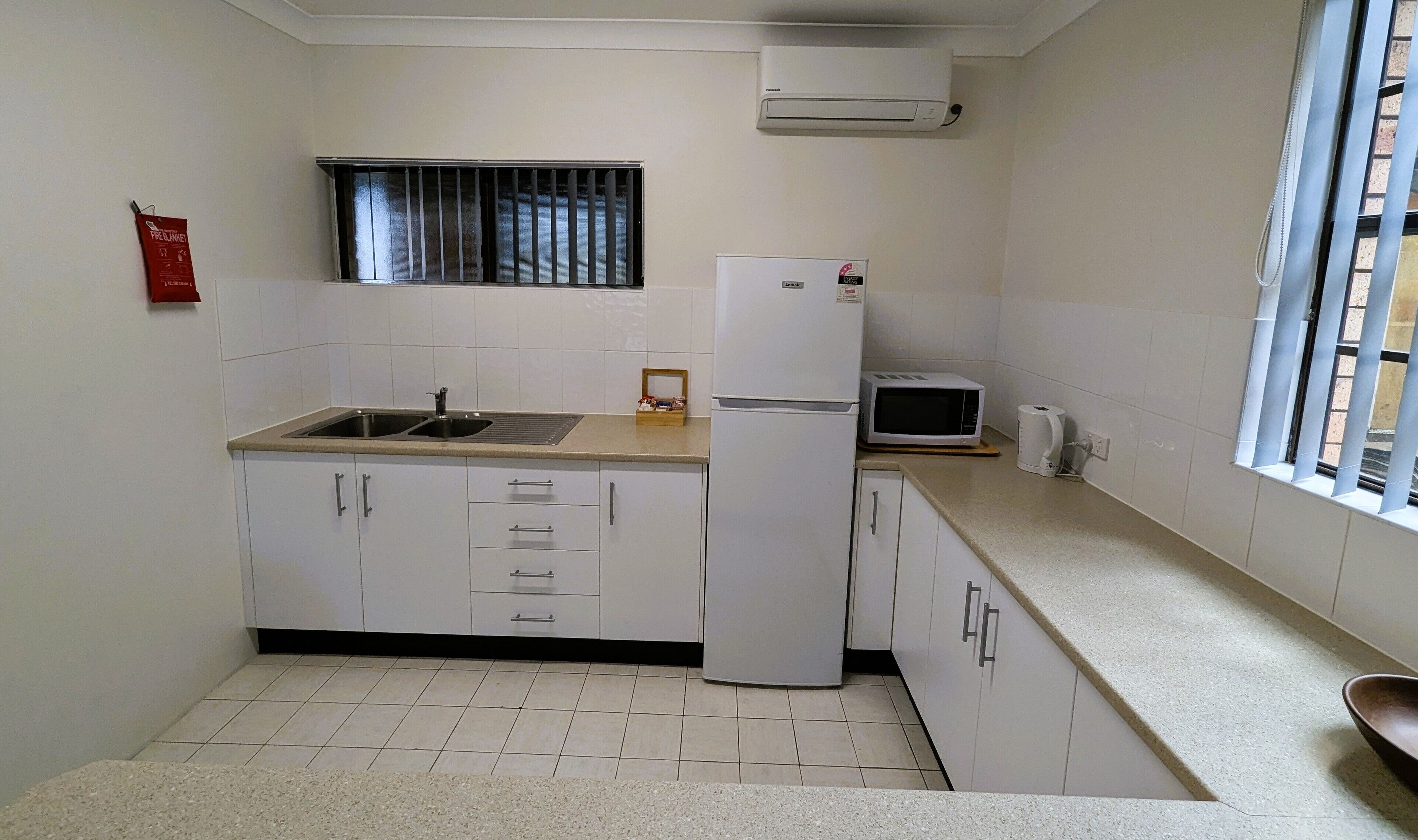 A compact kitchen with a sink, a refrigerator, a microwave, and a window with blinds.