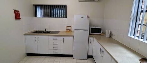 A compact kitchen with a sink, a refrigerator, a microwave, and a window with blinds.