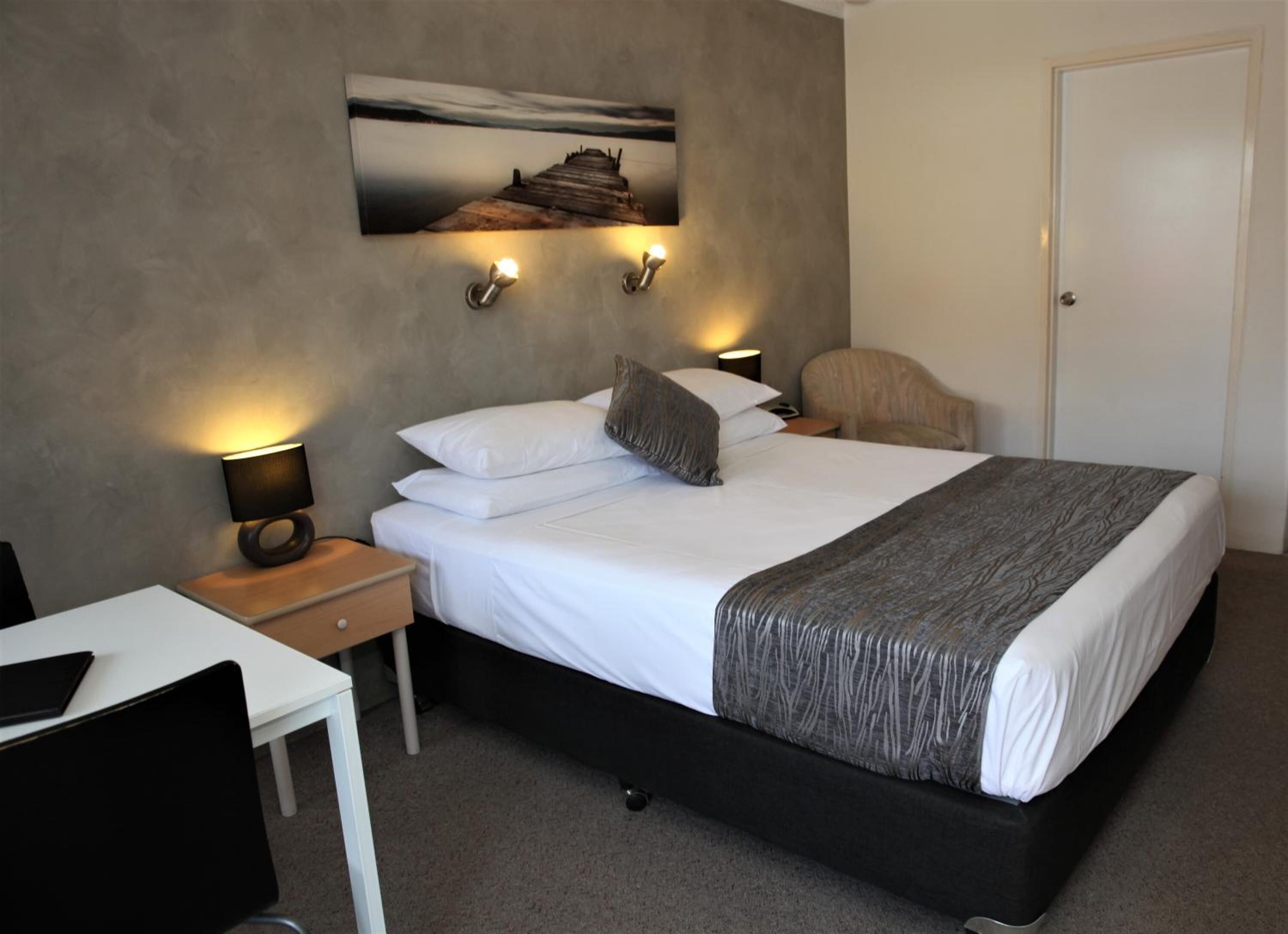 A hotel room with a bed, a desk, a chair, and a door.