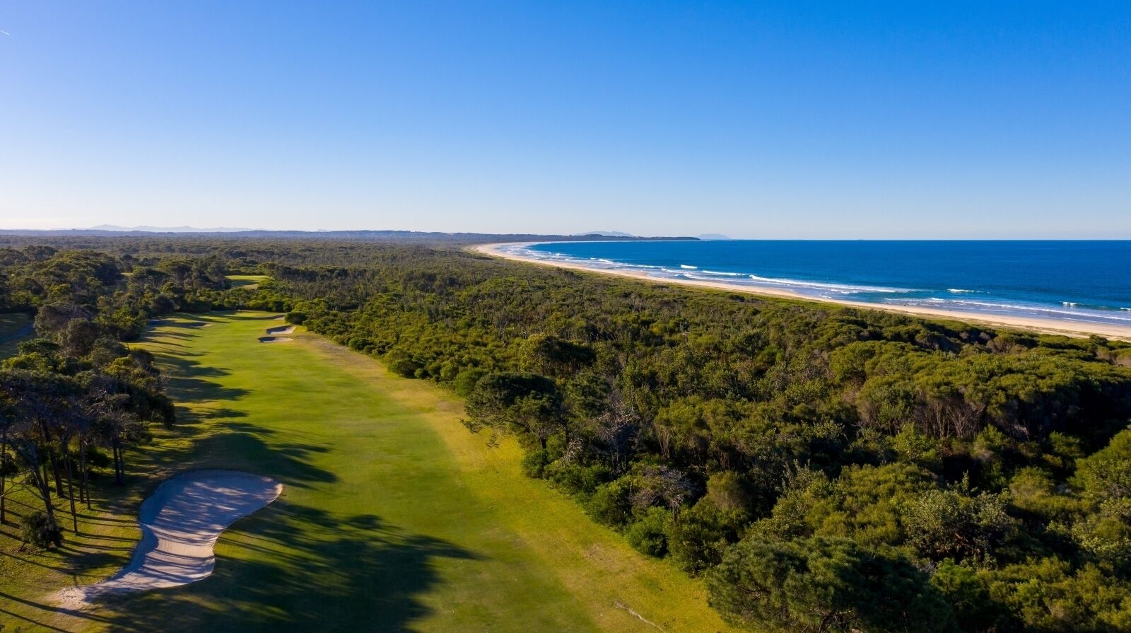 An aerial view of a golf course with a beach and forested area.