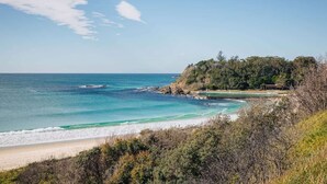 Un paisaje costero con playa, mar azul cristalino, afloramientos rocosos y abundante vegetación.