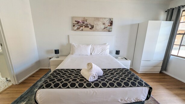 Un dormitorio ordenado con una cama grande, dos mesitas de noche, una obra de arte colgada en la pared y un armario.
