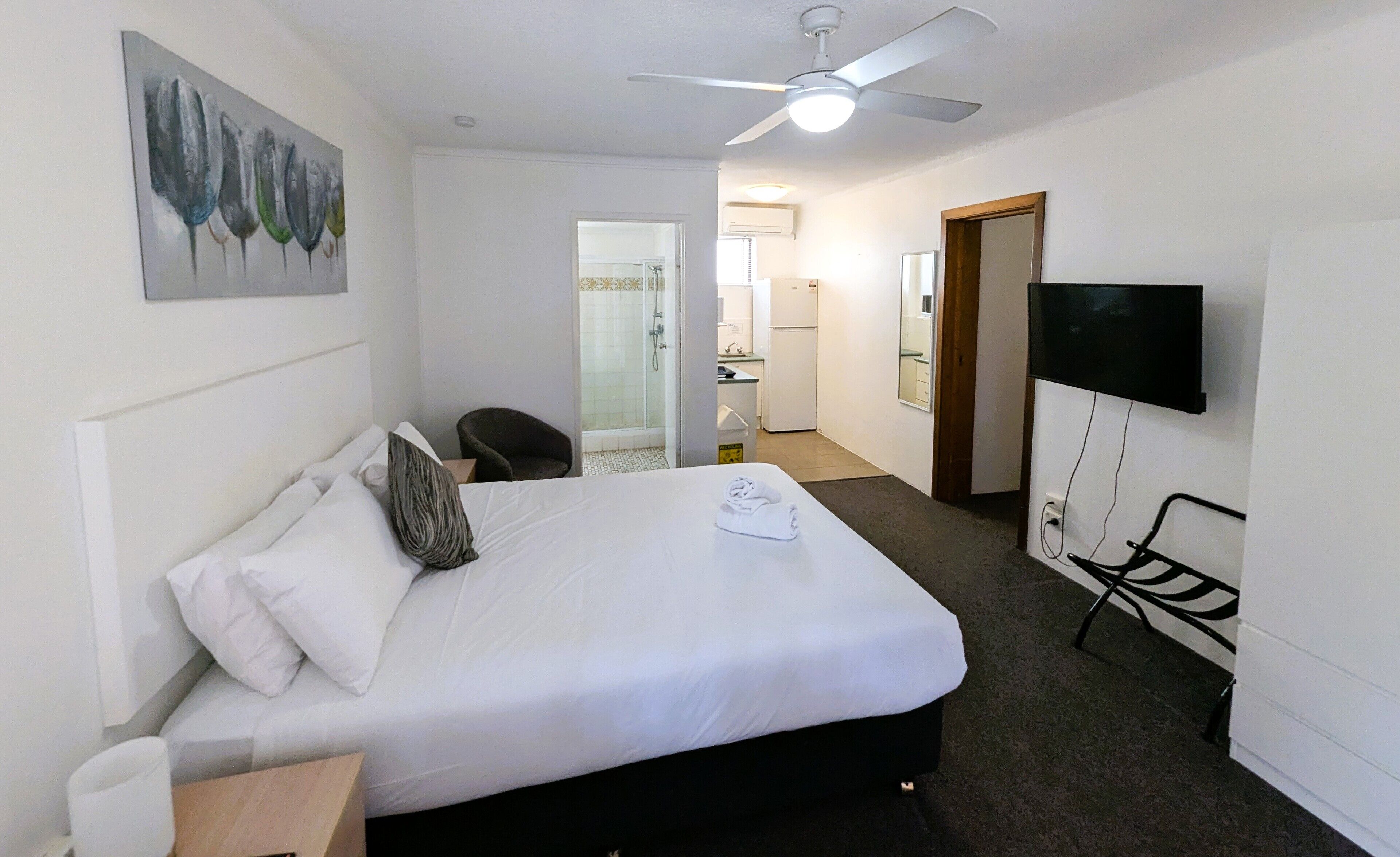 A hotel room with a bed, a ceiling fan, a TV mounted on the wall, and a bathroom visible through an open door.