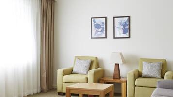 A hotel room with two armchairs, a small wooden table, and two framed artworks on the wall.