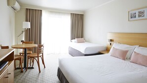 A hotel room with a bed, a desk, a chair, a lamp, and a window with curtains. - Bay Beach Motel (Byron Bay)