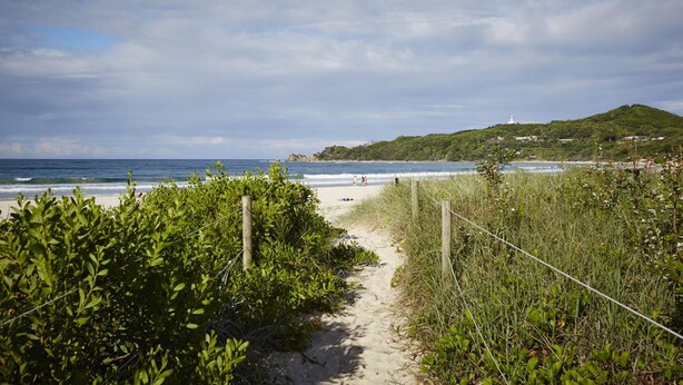 A beach path leading to the shore with a view of the ocean and a hill in the background. - Bay Beach Motel (Byron Bay)