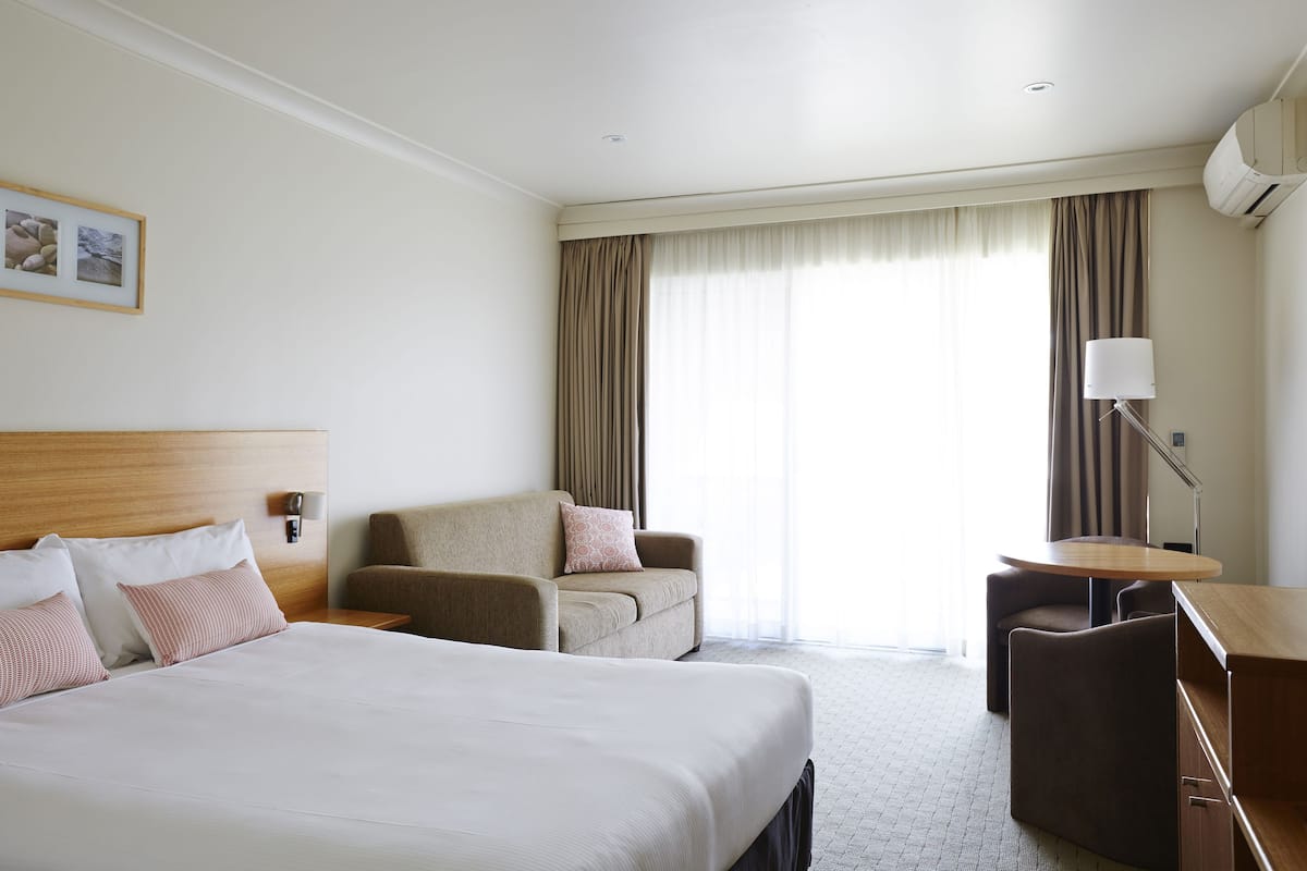 Una habitación de hotel con una cama grande, dos sillones, un escritorio y una lámpara.
