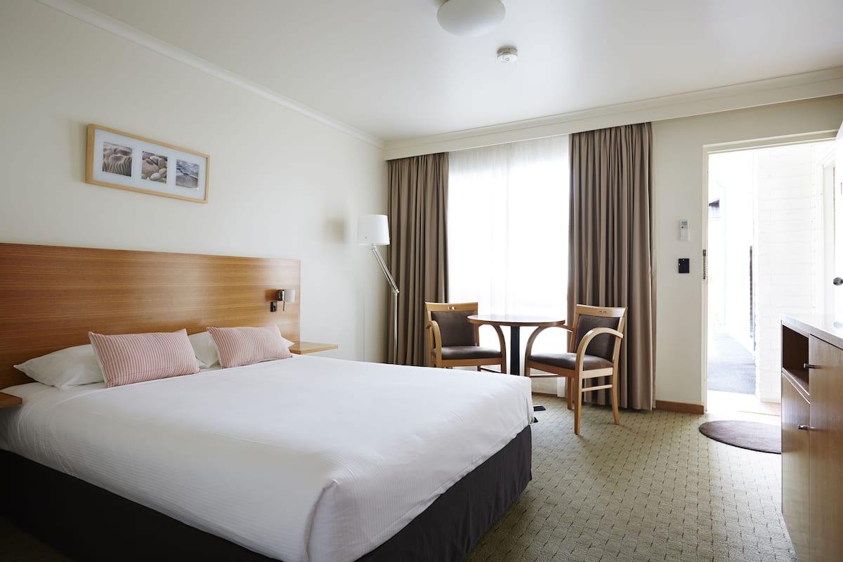 Habitación de hotel con una cama grande, un escritorio, dos sillas y una ventana con cortinas.