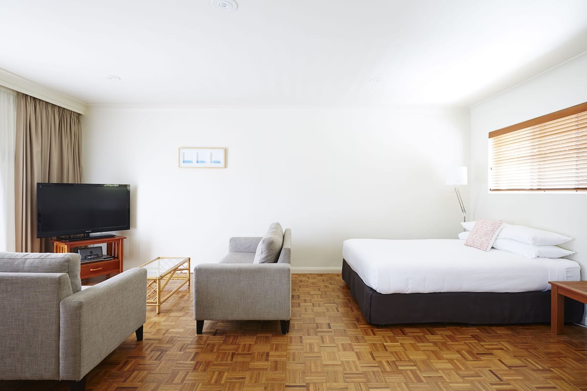 Una habitación de hotel con una cama, televisión, sofá y suelo de madera.
