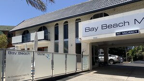 A motel named Bay Beach with a 'No Vacancy' sign, a covered parking area, and a sign indicating pool hours. - Bay Beach Motel (Byron Bay)