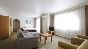 Una habitación de hotel con sofá, sillones, una mesa de madera, televisión y cama.