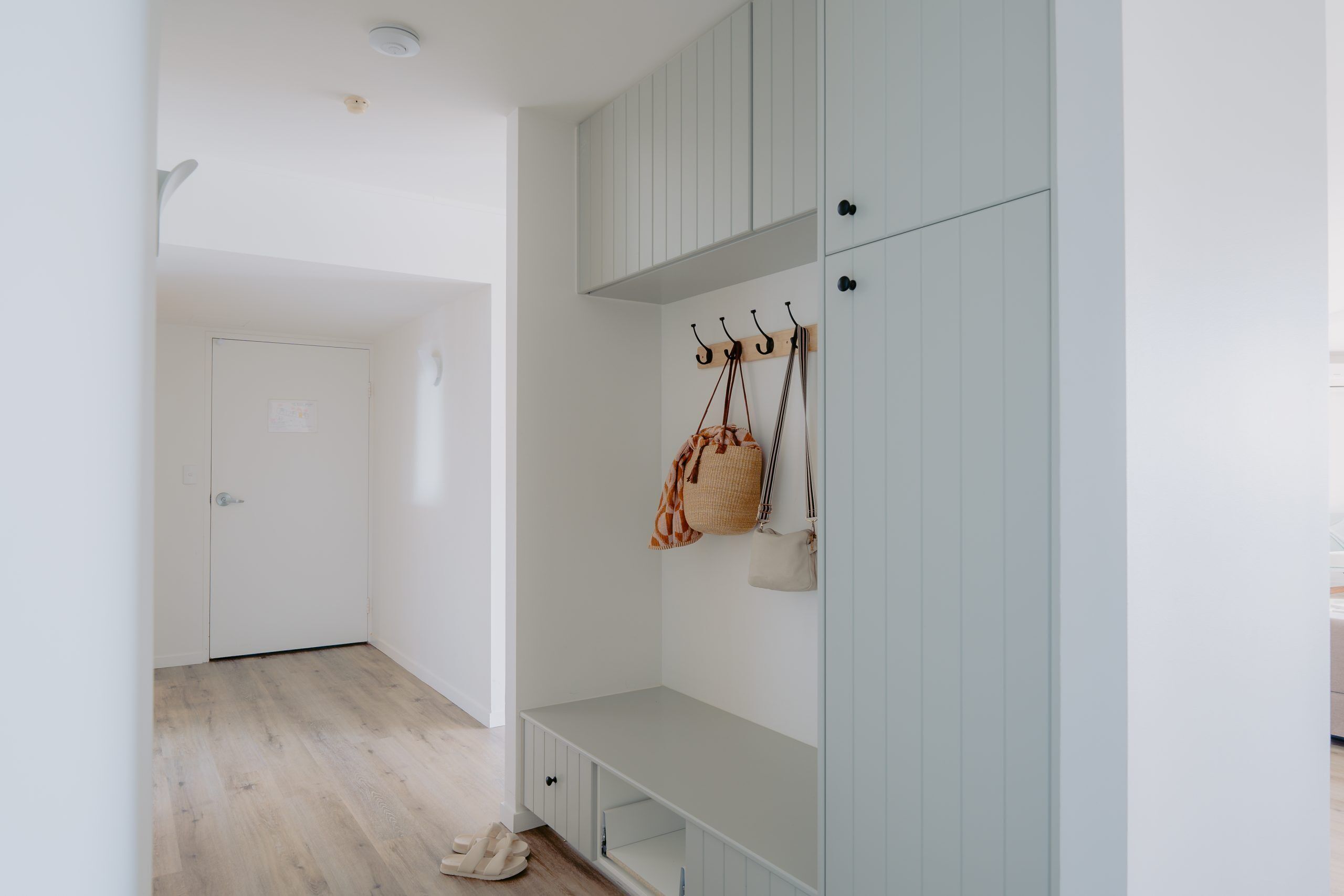 A hallway with a bench, a coat rack with bags, and a door.