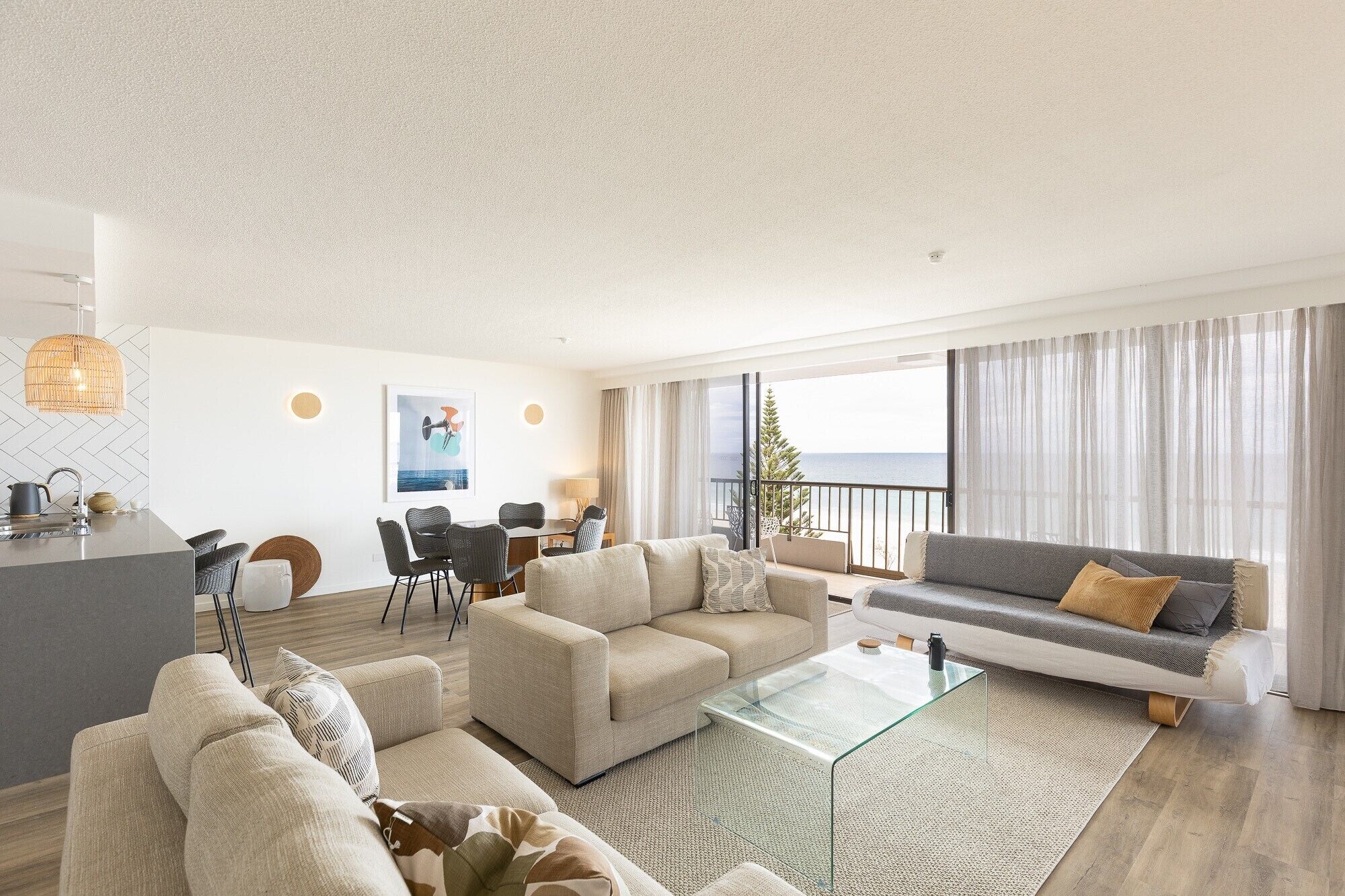 A modern living room with a sofa, armchairs, a glass coffee table, and a dining area with chairs and a table.