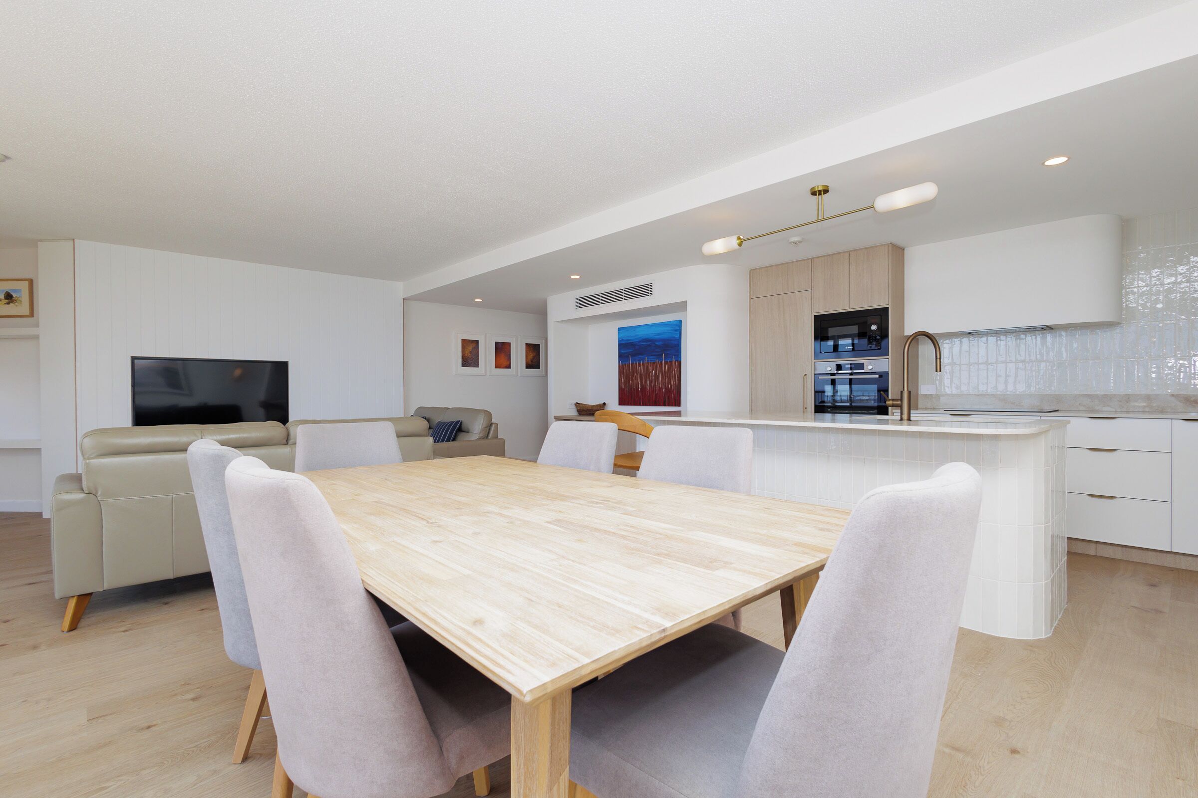 A modern kitchen with white cabinets, a wooden dining table, and a built-in oven.