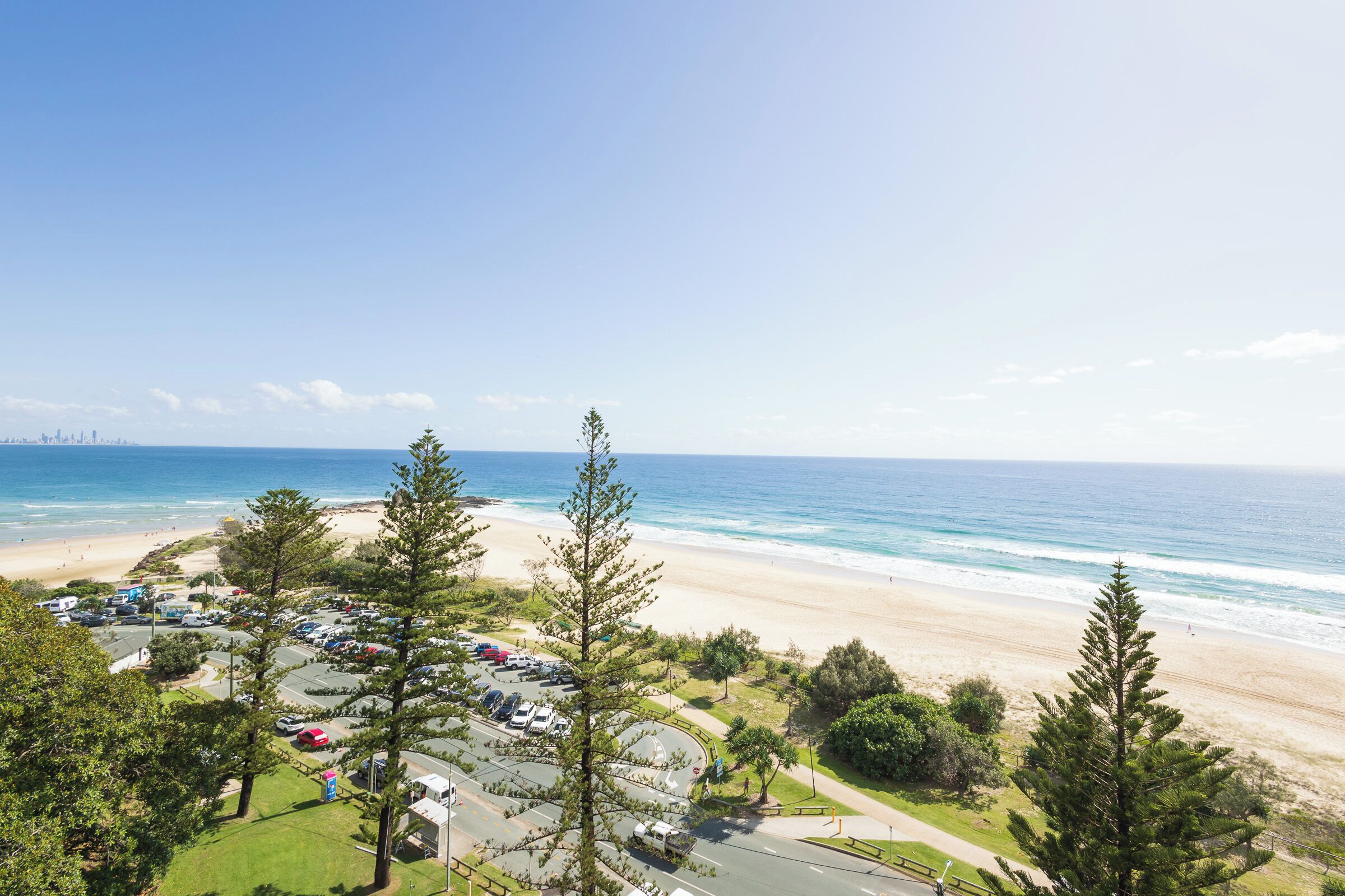 A coastal view with a beach, parking area, and trees.