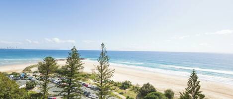 A coastal view with a beach, parking area, and trees.