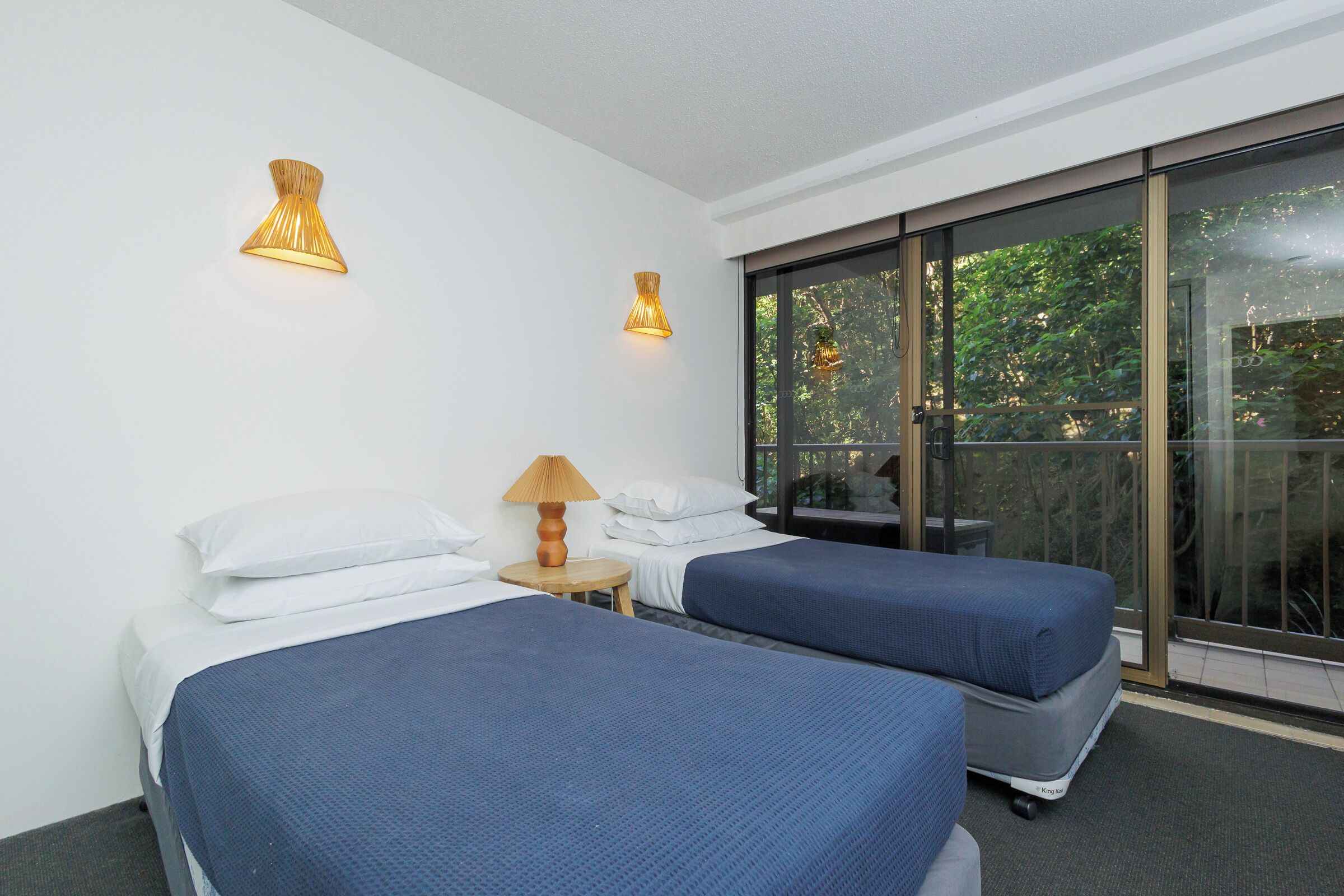 Une chambre d’hôtel avec deux lits, une petite table avec une lampe et une grande porte-fenêtre coulissante donnant sur l’extérieur.