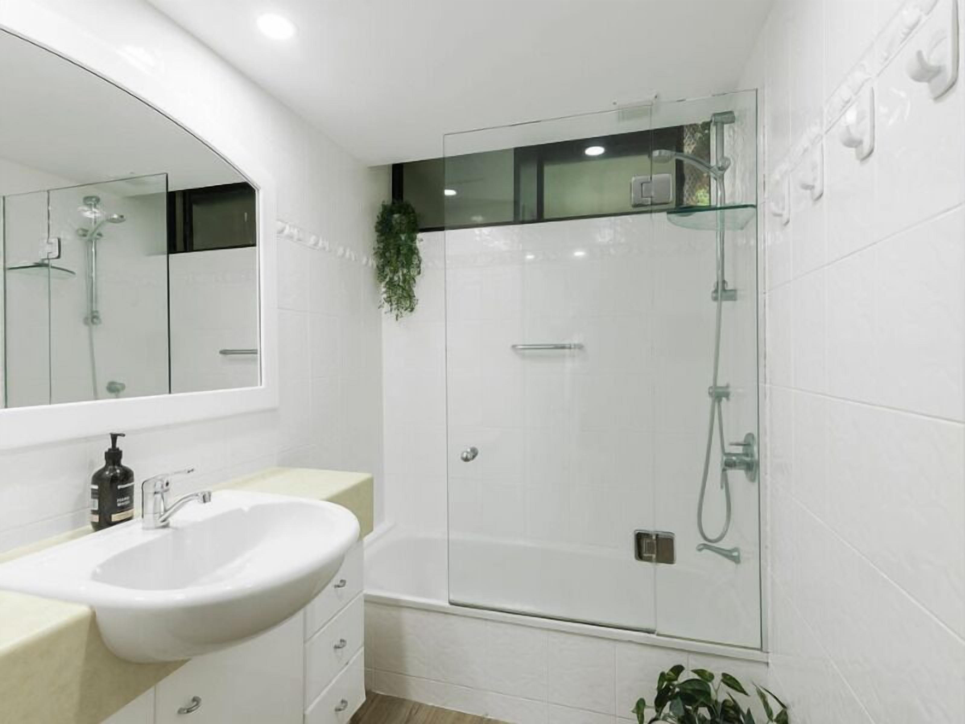 Une salle de bain moderne avec un lavabo blanc, un miroir et une cabine de douche en verre.