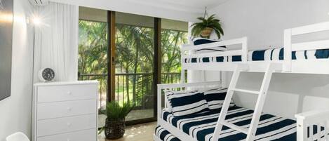 A modern bedroom with a bunk bed, a small desk, a chair, and a large window with a view of greenery.