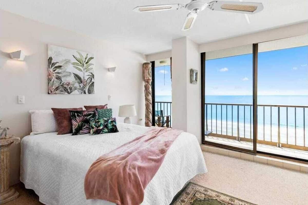 Une chambre dotée d’un grand lit, d’un ventilateur de plafond, d’une vue sur la plage et d’un balcon avec une balustrade.