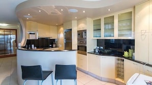 A modern kitchen with a curved island, two bar stools, and built-in appliances. - Seychelles on Main Beach (Main Beach)