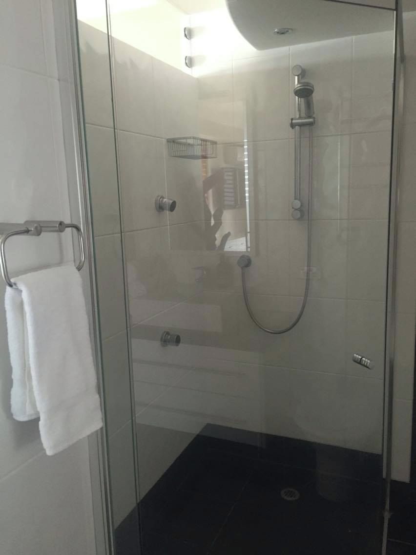 A glass-enclosed shower stall with a handheld showerhead and a wall-mounted faucet.