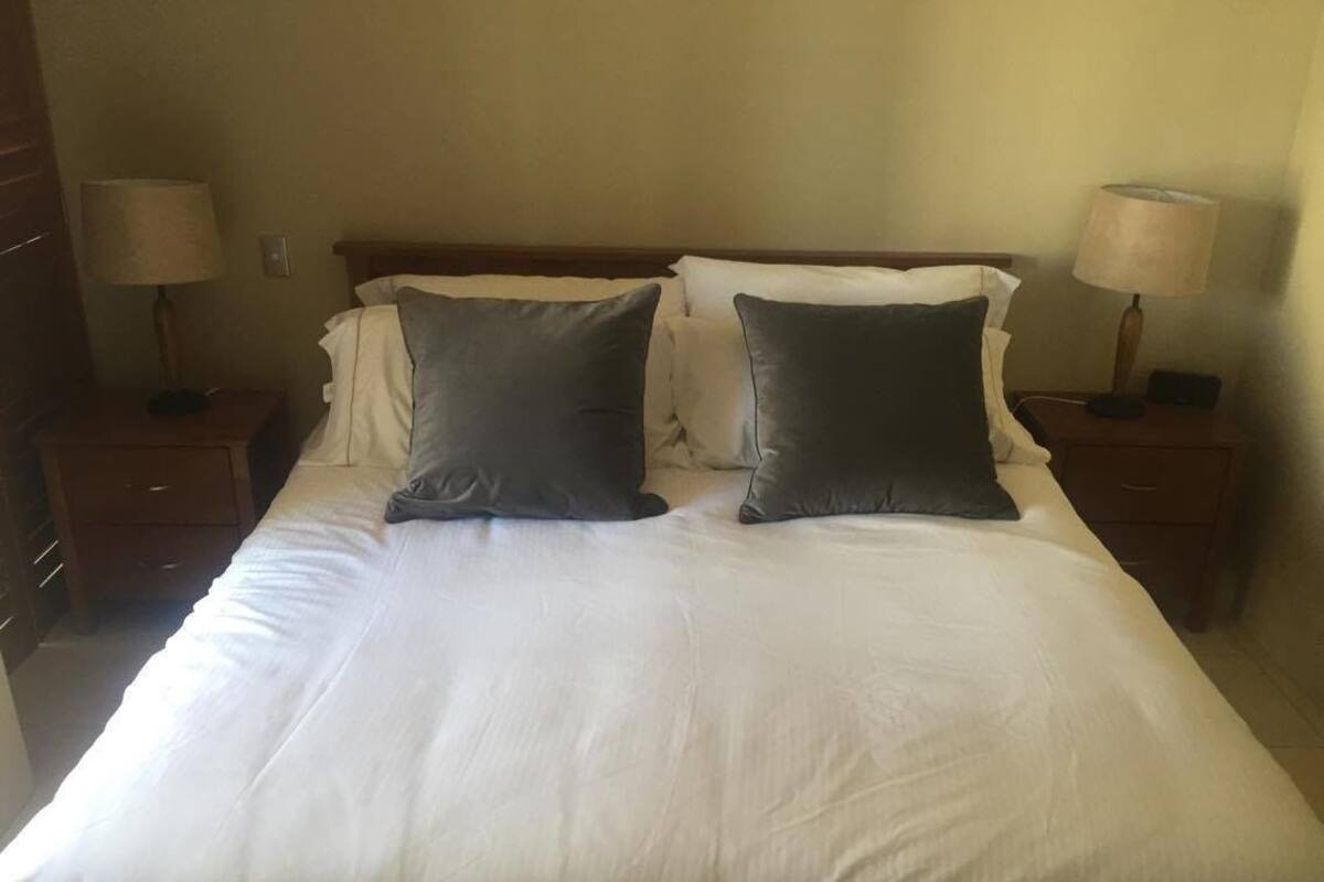 A neatly made bed with white linens and two dark pillows, flanked by two bedside tables with lamps.