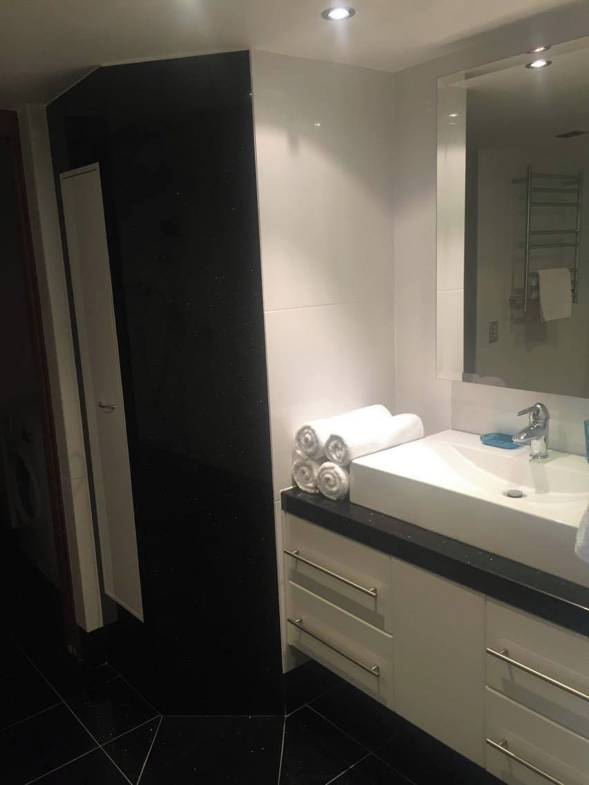 Un baño moderno con un lavamanos blanco, un espejo y una pared de acento negra.
