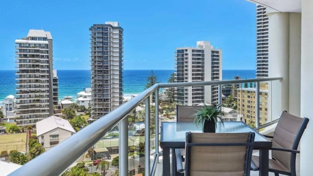 A balcony with a table and chairs, overlooking a coastal cityscape with tall buildings and the ocean. - Seychelles on Main Beach (Main Beach)
