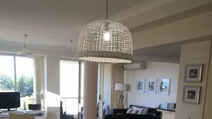 A modern dining area with a wooden table and white chairs, a hanging woven light fixture, and a view of the living room in the background. - Seychelles on Main Beach (Main Beach)