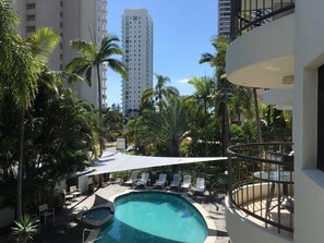 A pool area with lounge chairs and umbrellas, surrounded by palm trees and tall buildings. - Scalinada Apartments (Main Beach)
