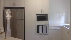 Eine kleine Küche mit einem Edelstahl-Kühlschrank, einer Mikrowelle und einem Backofen.