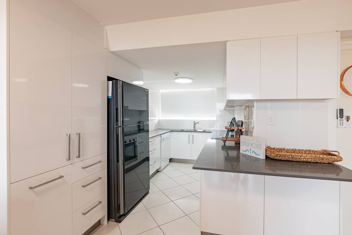 Eine moderne Küche mit weißen Schränken, einem schwarzen Kühlschrank und einem eingebauten Backofen.
