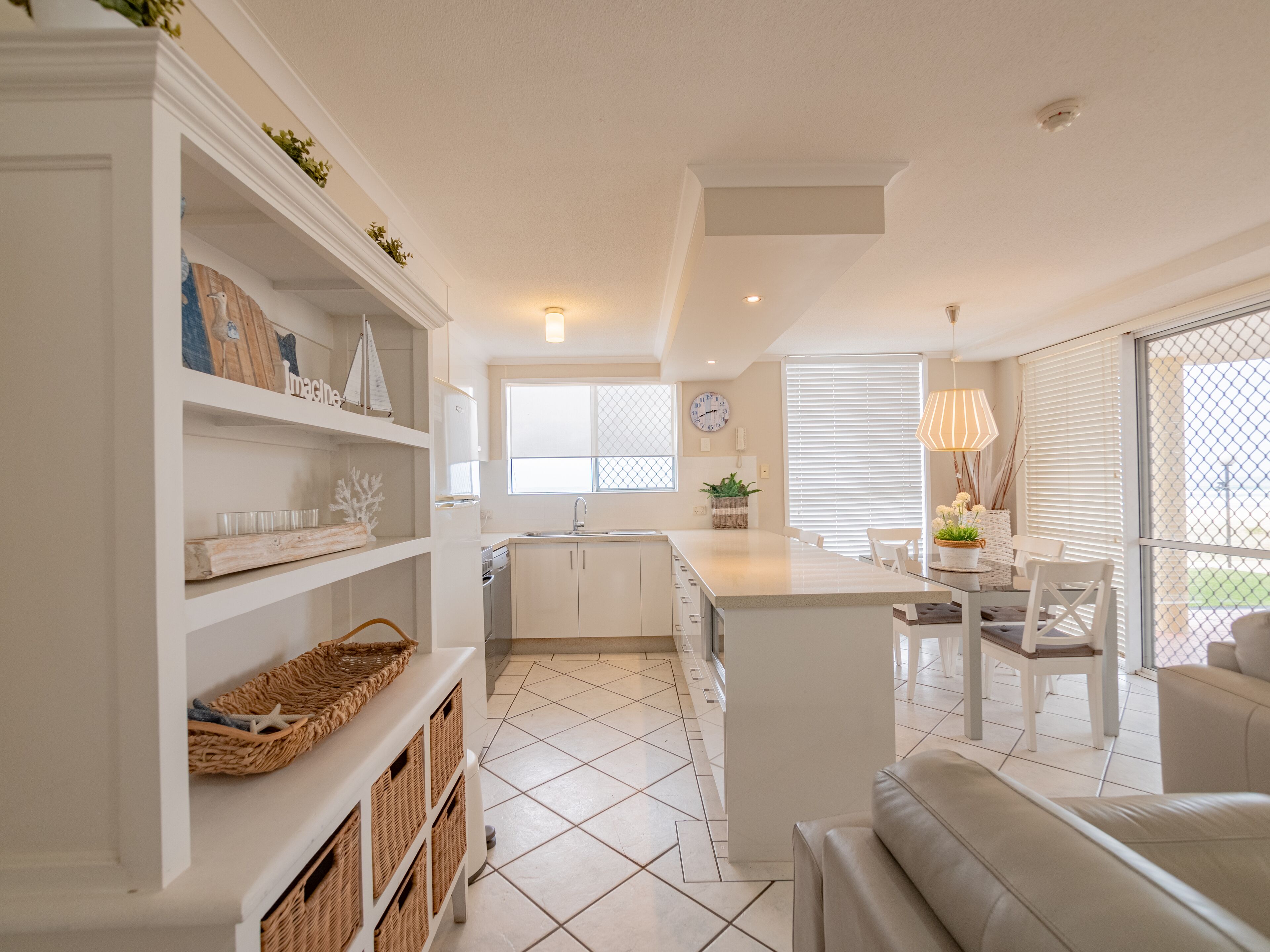 Una cocina moderna con armarios blancos, una isla central y una zona de comedor con mesa y sillas blancas.