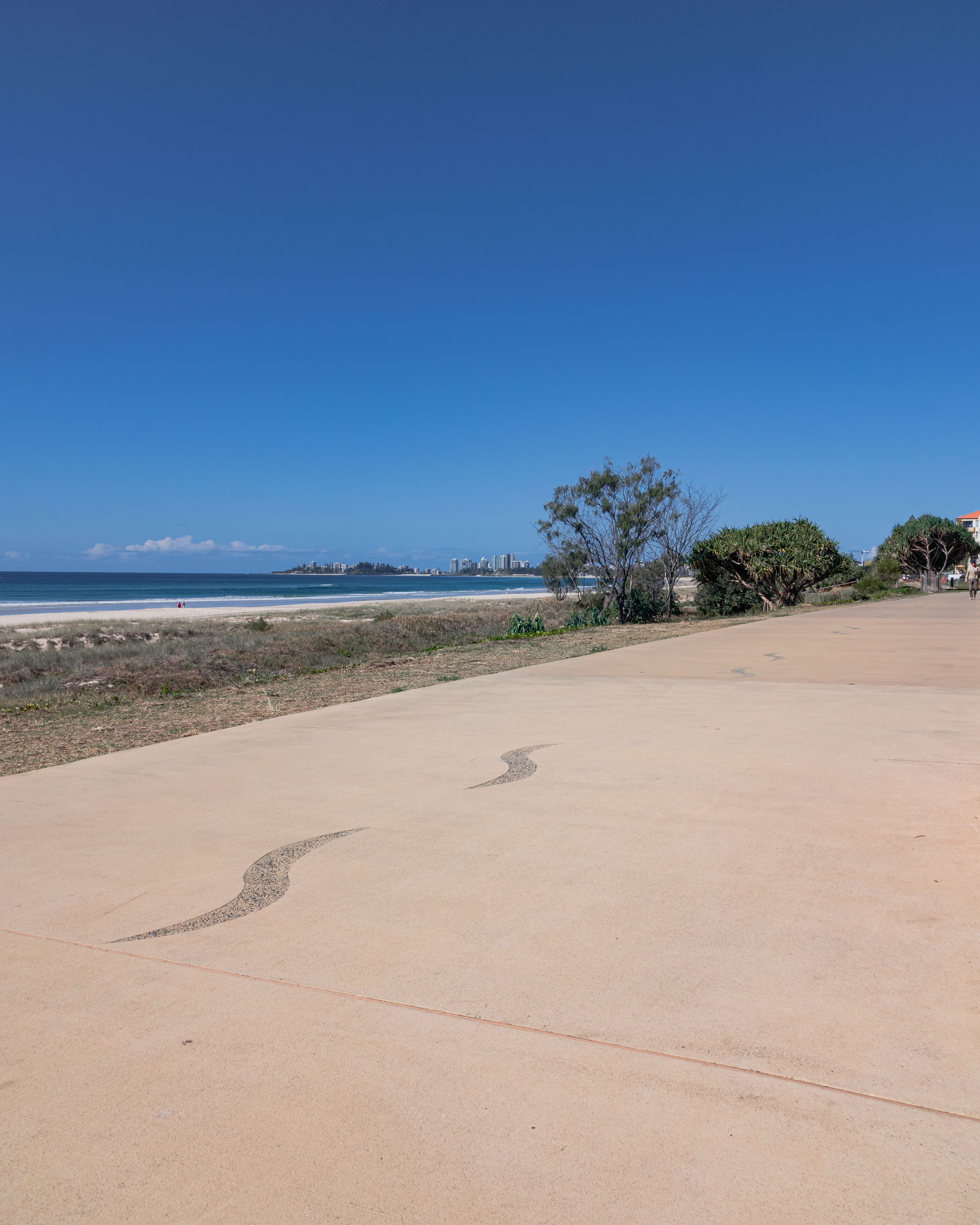 Ein weiter, offener Sandstrand mit blauem Himmel und einer entfernten Skyline.