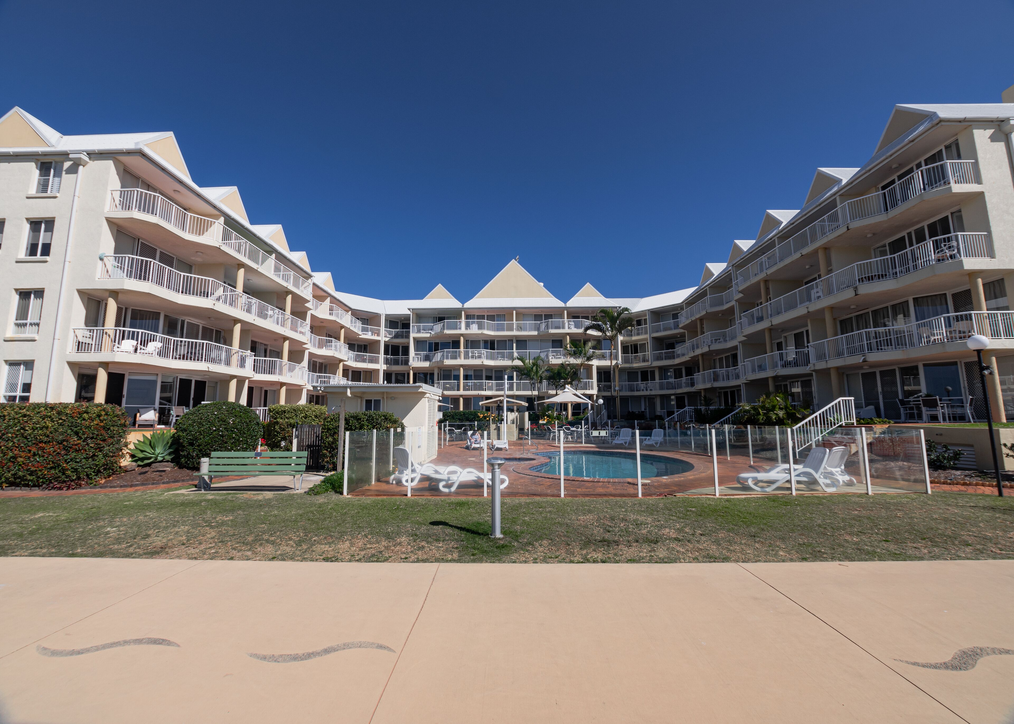 A multi-story hotel with balconies, a swimming pool, and outdoor seating areas.