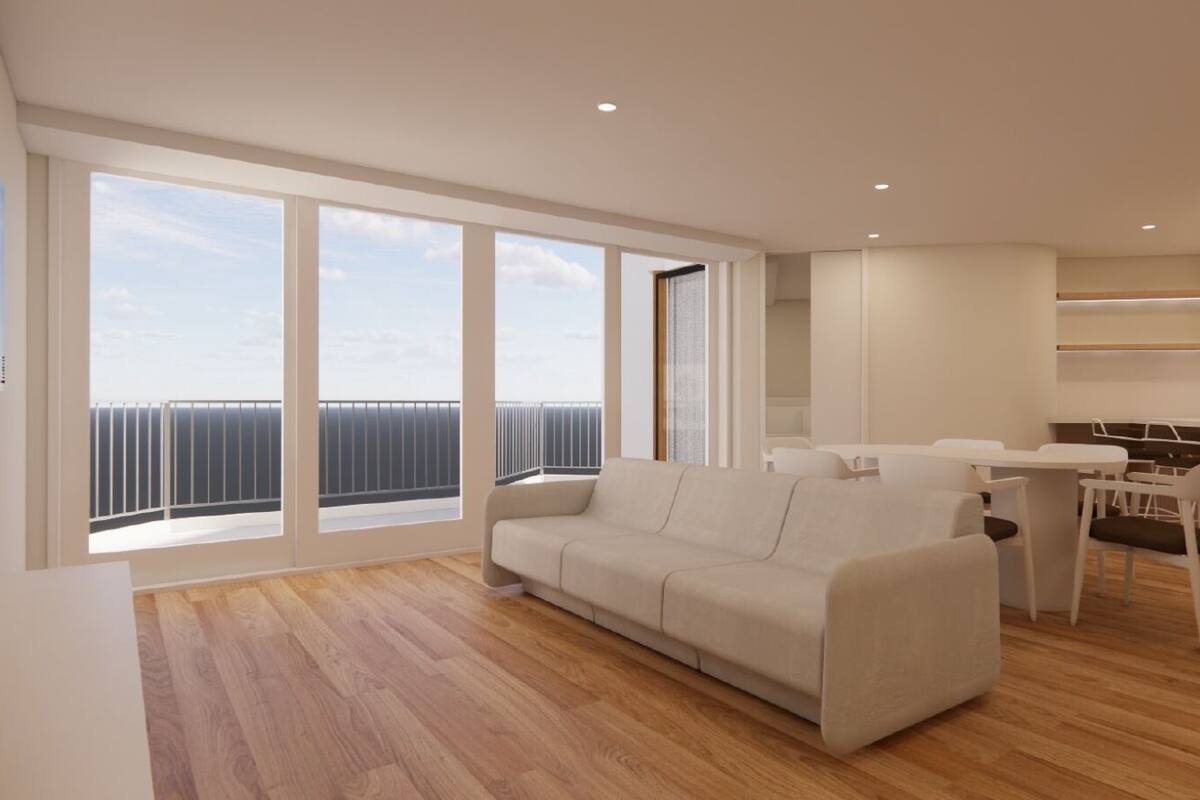 Ein modernes Wohnzimmer mit einer Couch, Esstisch und Stühlen. Große Fenster bieten Blick auf den Himmel und einen Balkon.