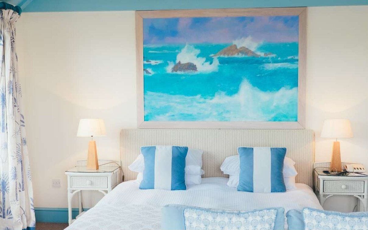 A hotel room with a large bed, two bedside tables, and a painting of the ocean on the wall.