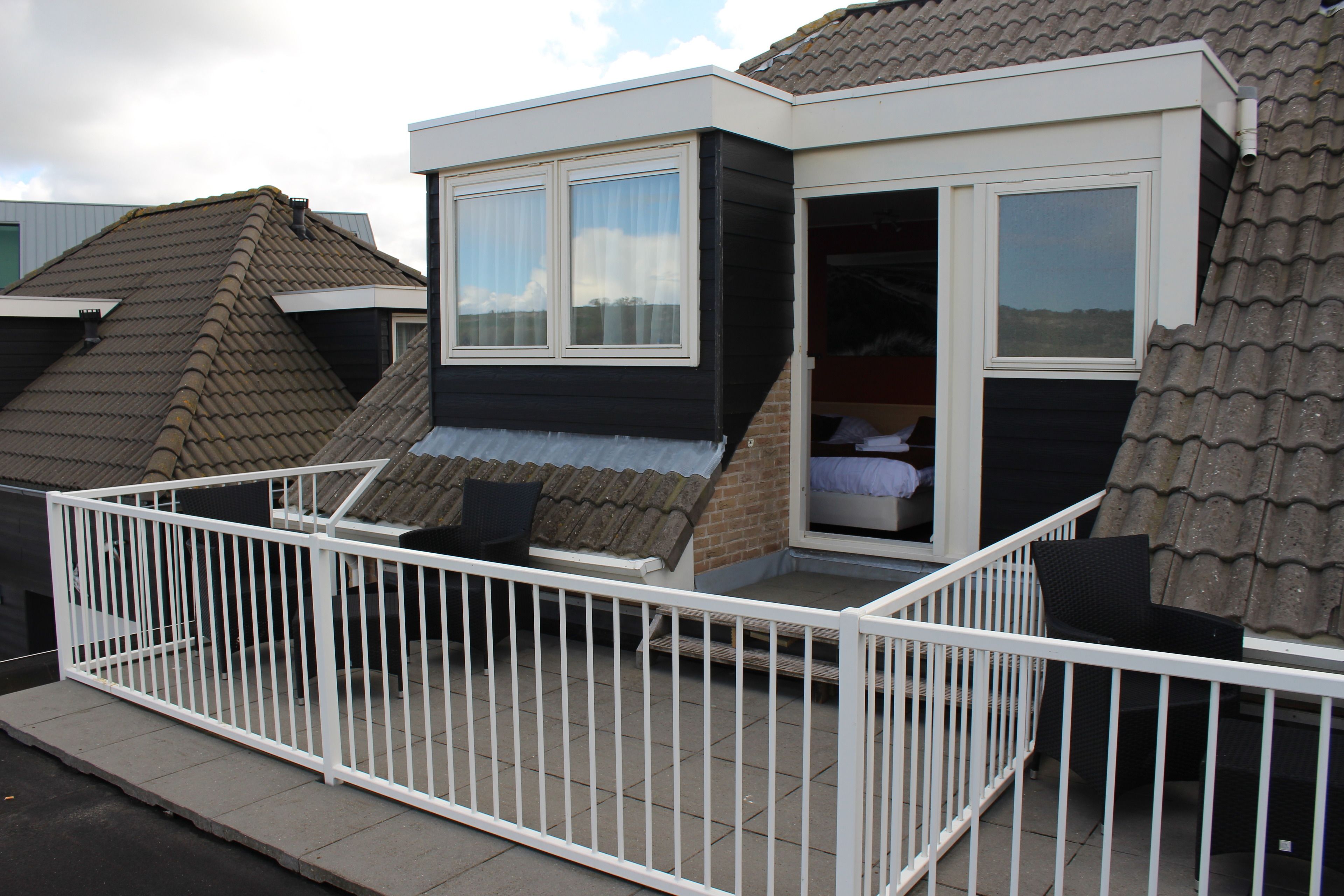 Een klein, modern huis met een balkon, een schuifdeur en een zichtbaar bed van binnen.