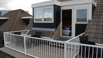 Een klein, modern huis met een balkon, een schuifdeur en een zichtbaar bed van binnen.