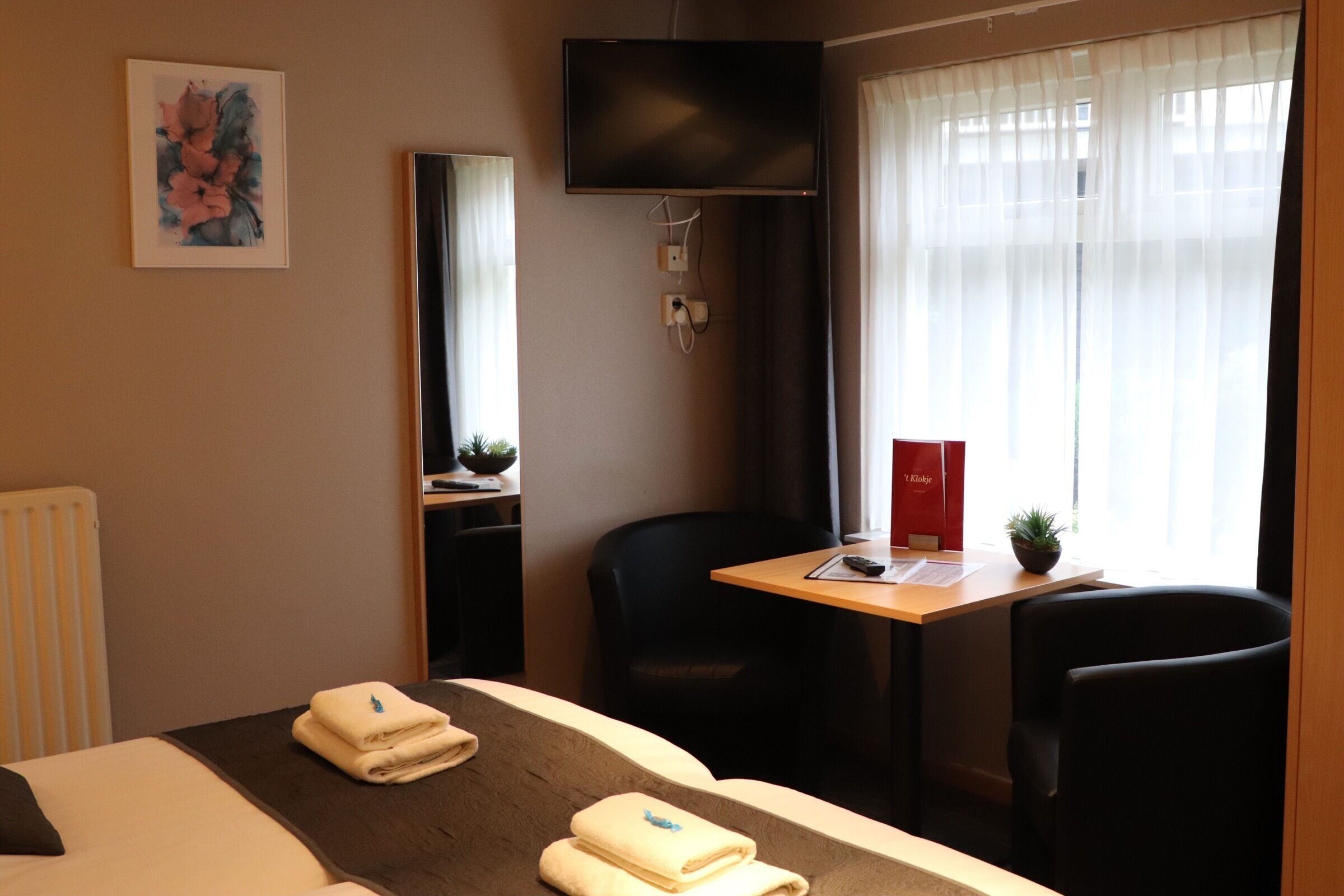 A hotel room with a bed, a desk, a chair, a TV, and a window with curtains.