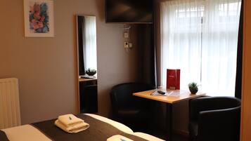 A hotel room with a bed, a desk, a chair, a TV, and a window with curtains.