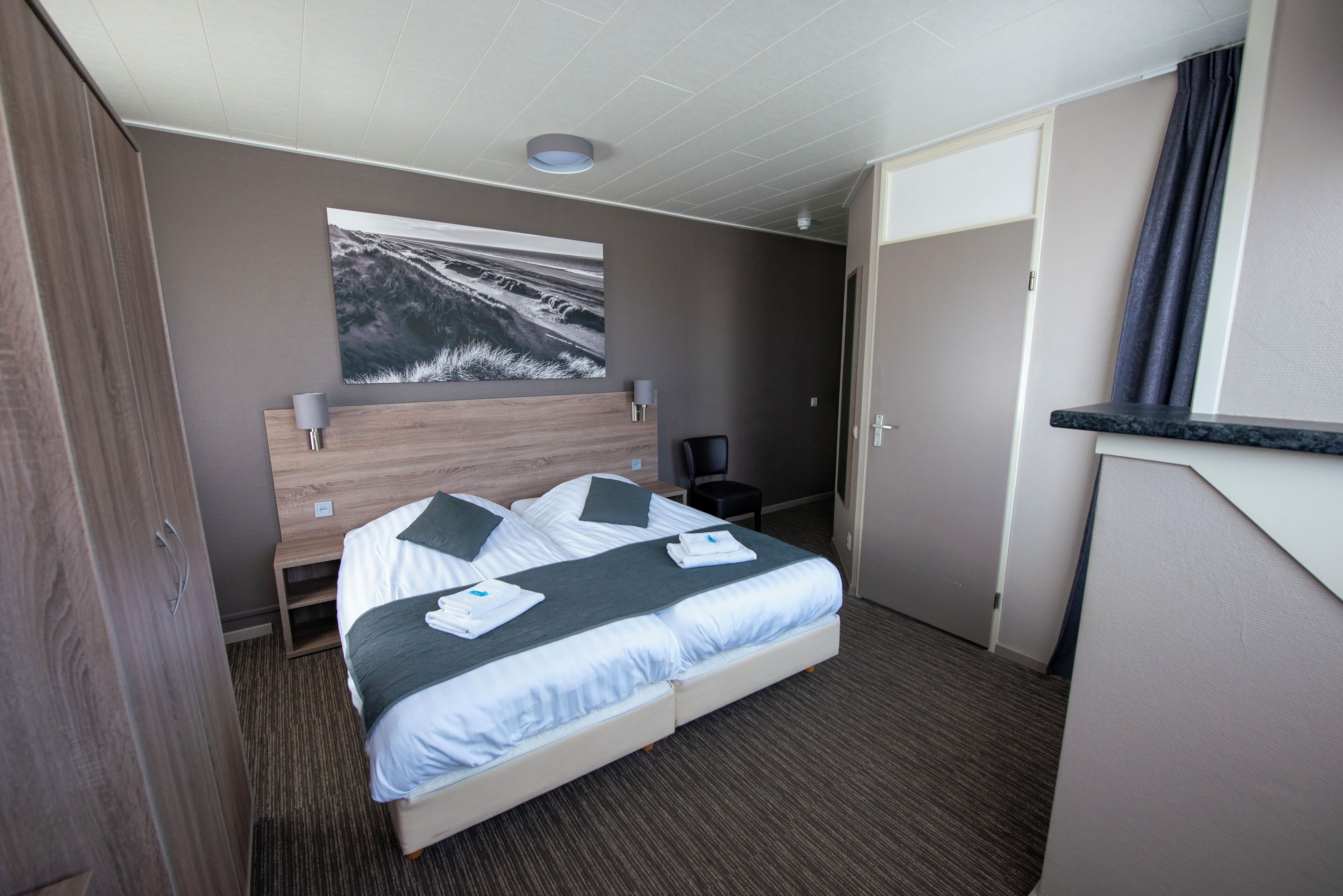 Een hotelkamer met een bed, een bureau, een stoel, een schilderij aan de muur en een deur.