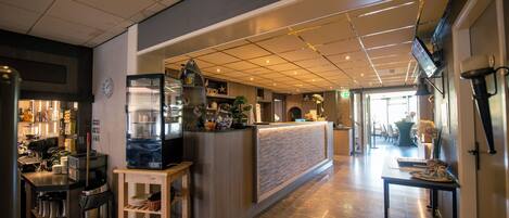A modern hotel lobby with a reception desk, a coffee machine, and a seating area.